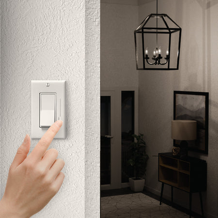 Hand pressing a light switch in a dimly lit room with a chandelier.