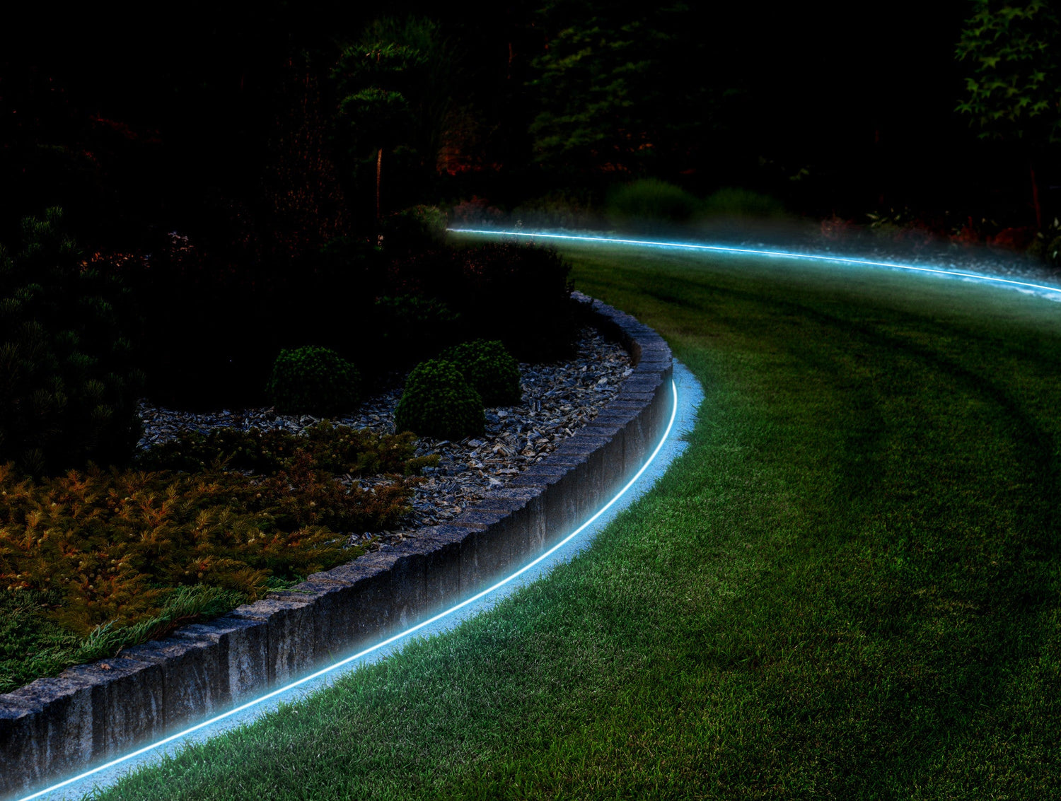 Curved garden path illuminated by a strip of glowing blue lights at night.